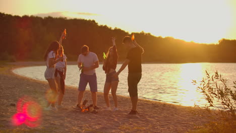 The-students-celebrate-end-of-educational-year-on-the-open-air-party-on-the-lake-coast-with-beer.-It-is-crazy-and-hot-beach-party-between-the-best-friends-around-bonfire.
